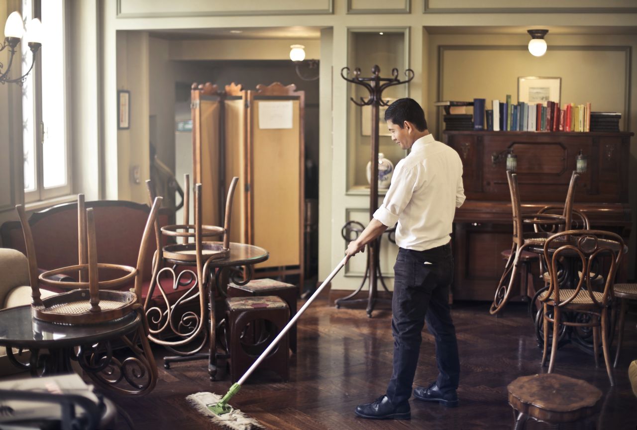 Side view of a young ethnic man in uniform mopping the floor while working in a retro-style restaurant